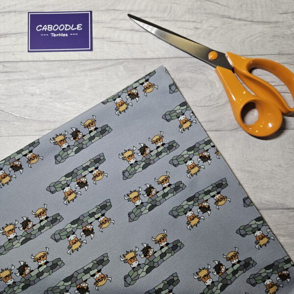 Grey background fabrics with cartoon style highland cows leanigng over a stone wall