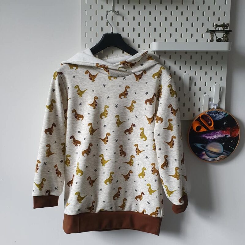 a hoodie made from alpine fleece showing a golden dinosaur on a cream background.
