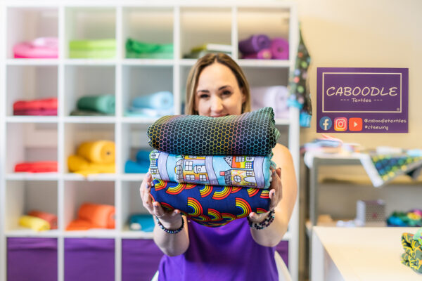 A lady holds a stack of brightly coloured fabrics