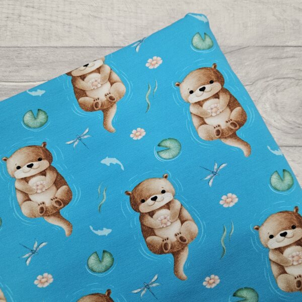 Downstream Jersey Fabric shows an adorable otter floating on their back in a stream of water lilies. This fabric has a bold turquoise background which gives a joyful water effect.