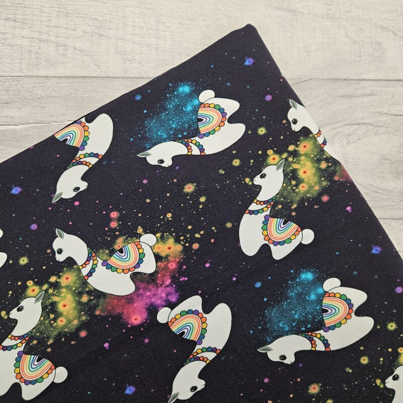 Cosmic Llama Jersey Fabric is a joyful design with a multi directional llama floating over a galaxy space themed background